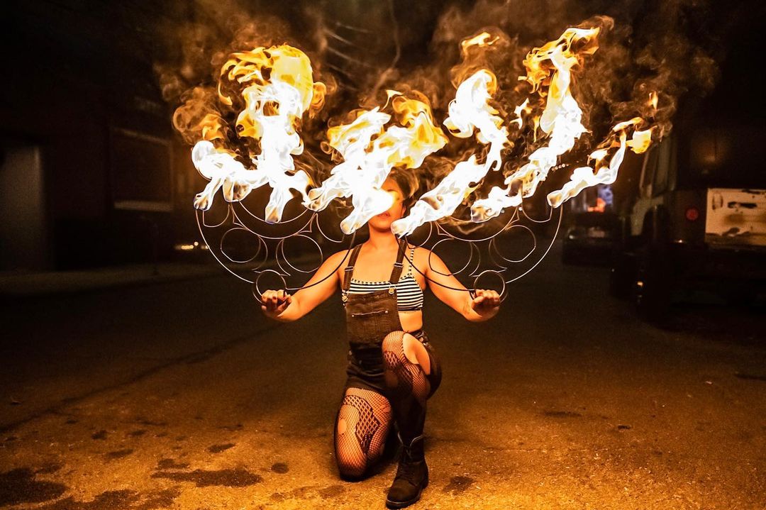 A woman holds two burning fire fans