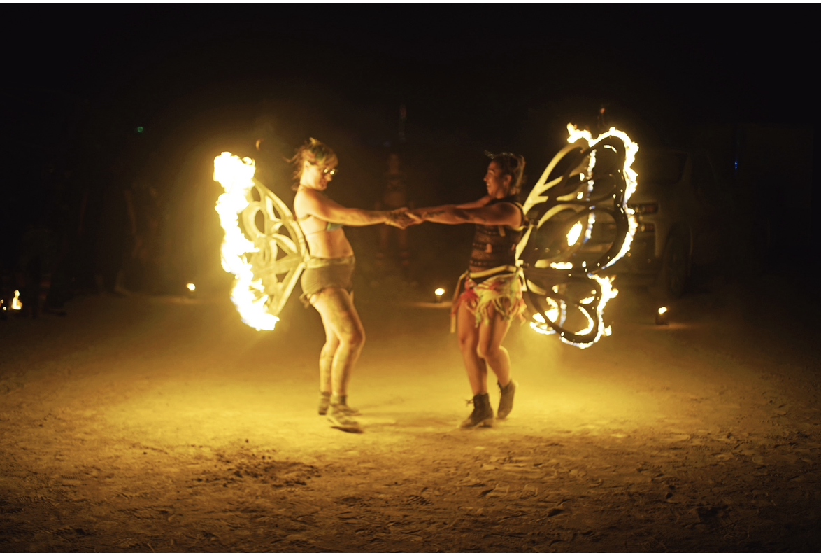 Two women with flaming butterfly wings dance